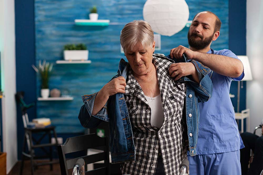 Healthcare worker helping an older woman put on a jacket